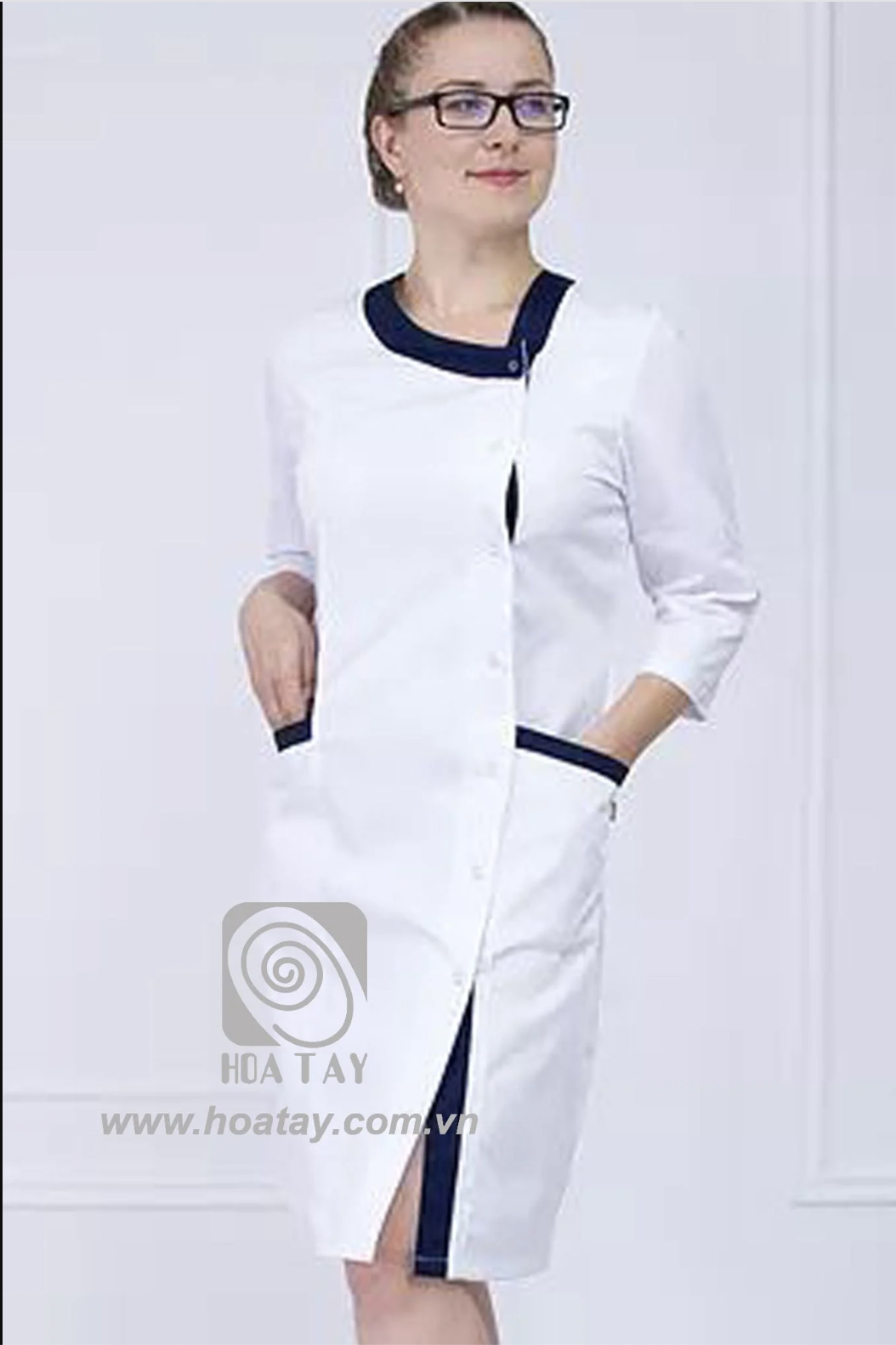 Một nữ nhân viên y tế đang đứng, mặc áo blouse trắng (áo khoác phòng thí nghiệm) cổ tròn phối viền xanh navy, tay lỡ, cài khuy lệch, có hai túi hông, trên nền trắng sáng.