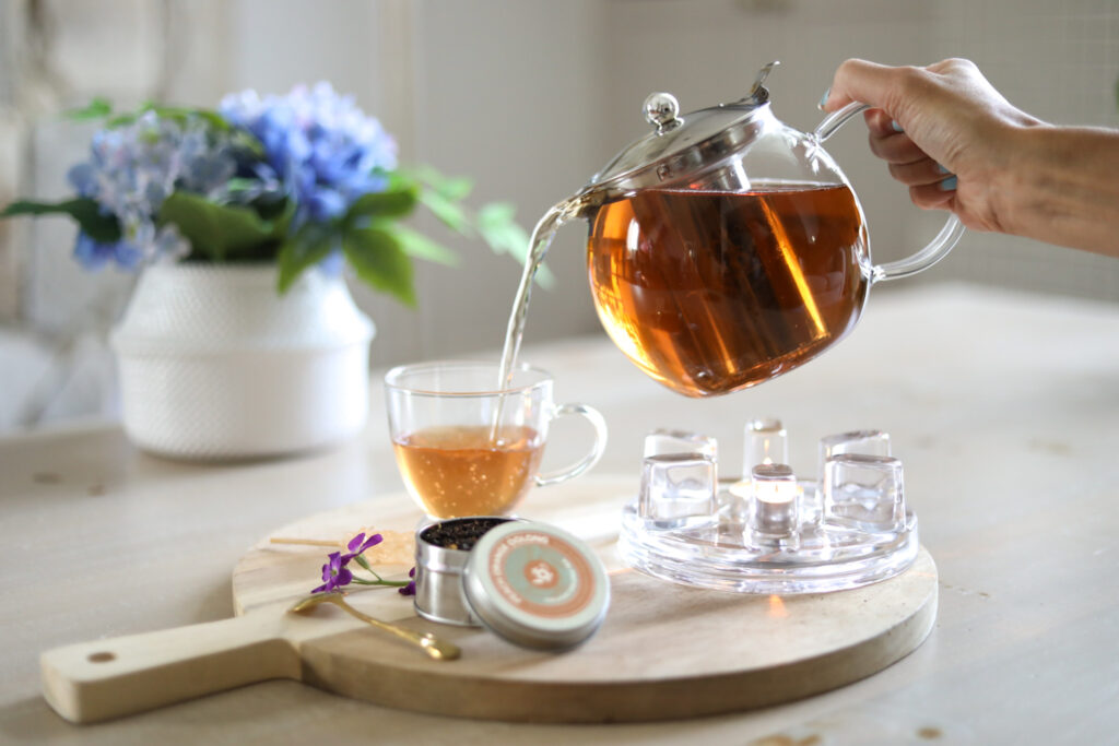 Hình ảnh một người đang rót trà thảo mộc hỗ trợ giấc ngủ từ ấm thủy tinh vào cốc, thể hiện sự tiện lợi của liệu trình Lục Lam.