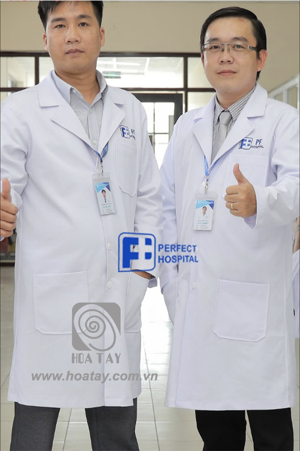 Hai bác sĩ nam đang đứng, giơ ngón cái biểu thị sự hài lòng. Họ mặc áo blouse trắng (áo khoác phòng thí nghiệm) dài tay, cổ bẻ (cổ ve), có túi vuông phía trước, chất liệu vải phẳng, logo thêu ngực trá