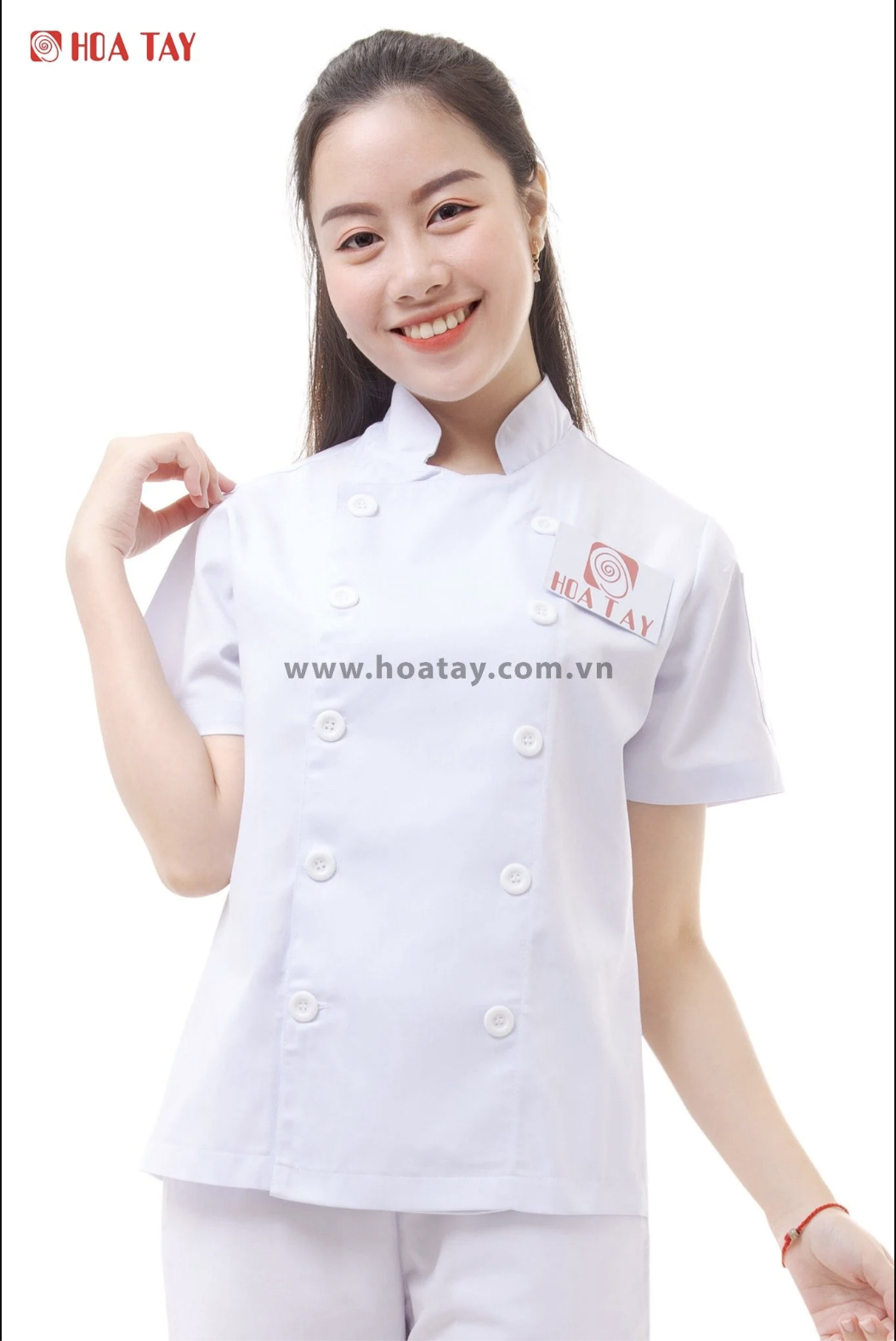 Một nữ nhân viên đang mỉm cười, mặc áo bếp trắng tay ngắn, kiểu cài khuy kép (hai hàng nút), cổ đứng, chất liệu vải phẳng mịn, logo Hoa Tay trên ngực, nền trắng studio ánh sáng đều.