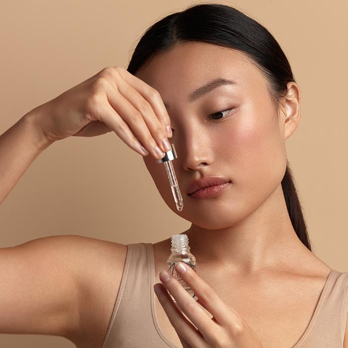 Một phụ nữ châu Á đang thoa serum lên mặt, biểu trưng cho việc bổ sung hoạt chất vào routine chăm da đơn giản.