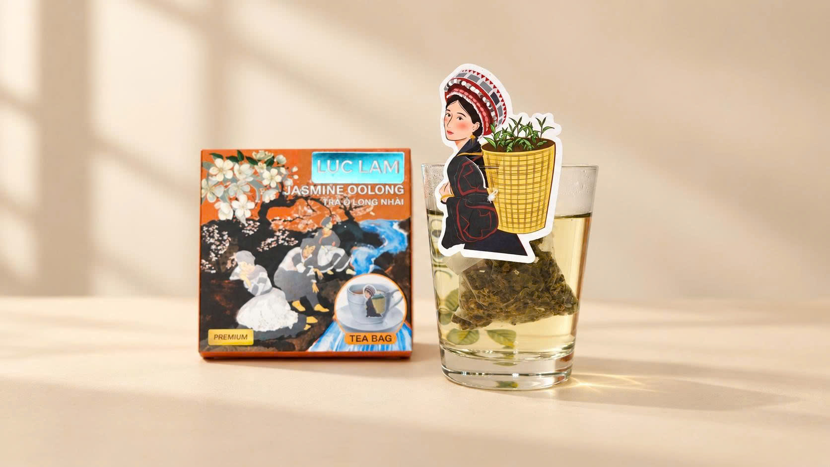 One box of Luc Lam Jasmine Oolong tea and one glass of brewed tea. The box has an orange and black label with a traditional Vietnamese painting of women in white dresses and a jasmine flower branch. T