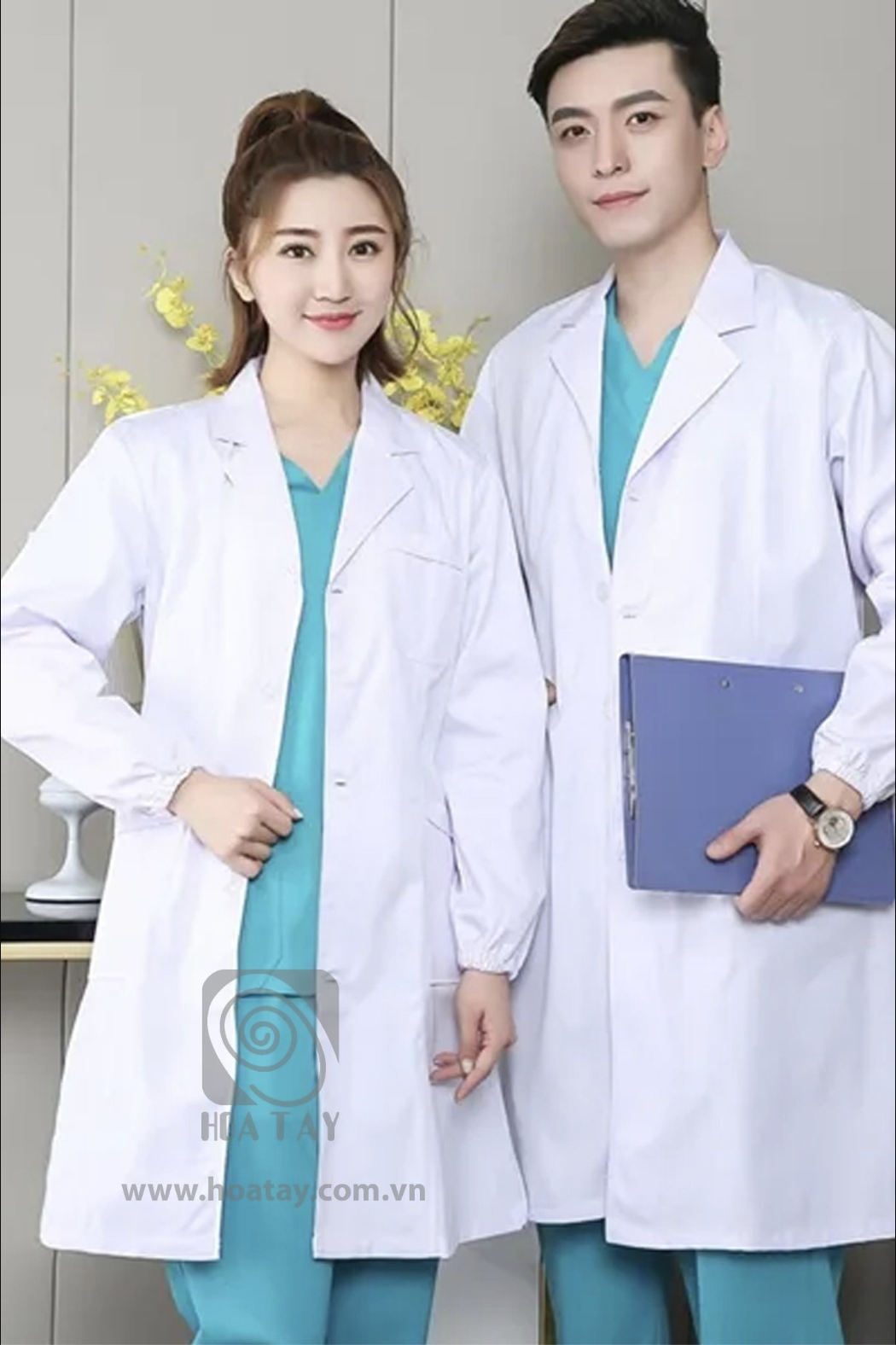 Hai nhân viên y tế (một nam, một nữ) đang đứng, mặc áo blouse trắng (áo khoác bác sĩ) cổ bẻ, tay áo bo chun (cổ tay co giãn), chất liệu vải phẳng, bên trong là bộ scrub xanh ngọc, bối cảnh studio với