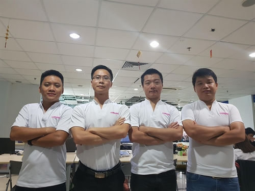Một người lớn và bốn trẻ em đang nấu ăn; mặc áo thun vàng, tạp dề trắng (tấm vải che trước ngực) và mũ đầu bếp vải; bối cảnh bếp hiện đại, ánh sáng tự nhiên.