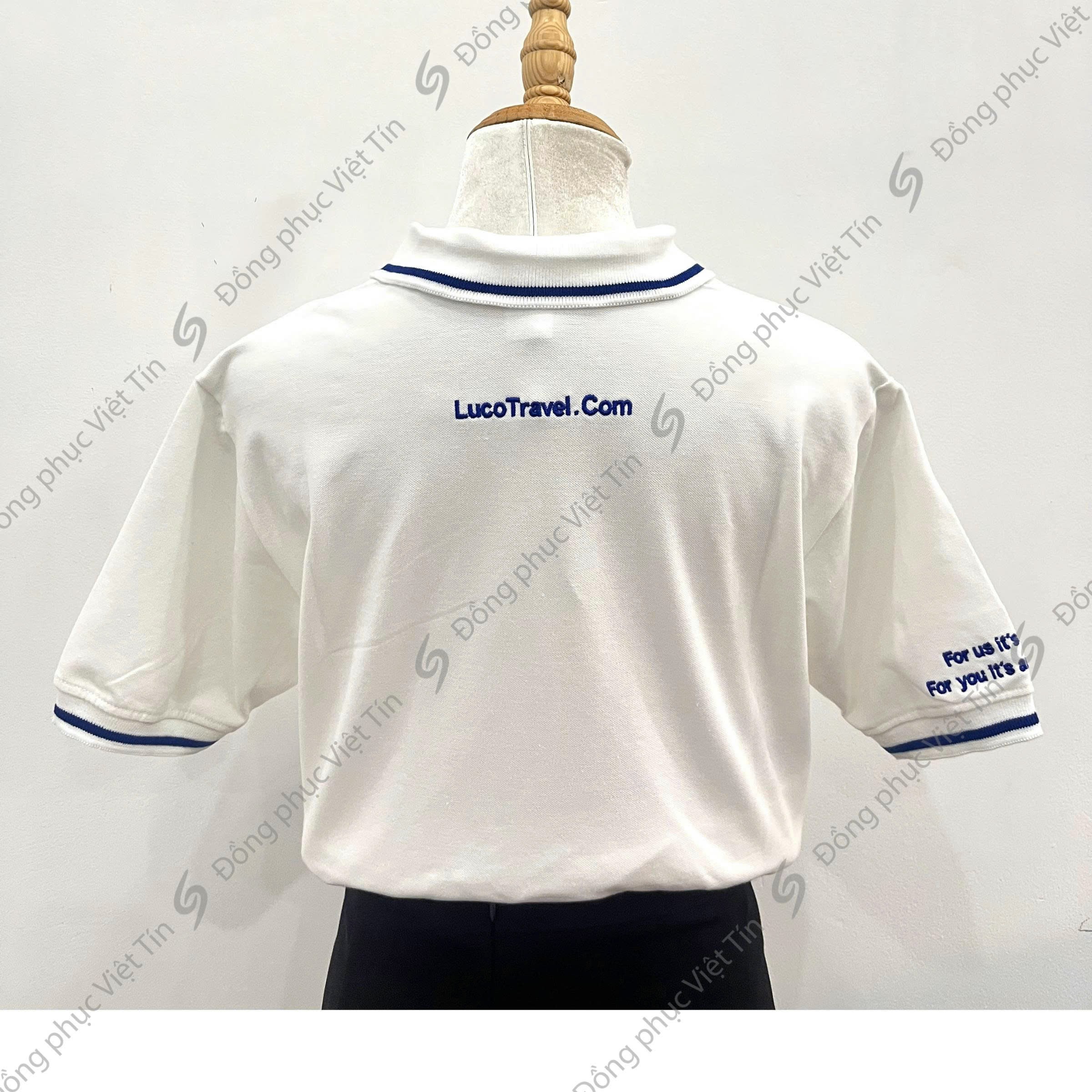 Áo polo màu trắng có cổ và tay áo viền xanh dương, mặt sau in logo LucoTravel.com và dòng chữ thêu ở tay áo, được trưng bày trên ma-nơ-canh trên nền trắng.