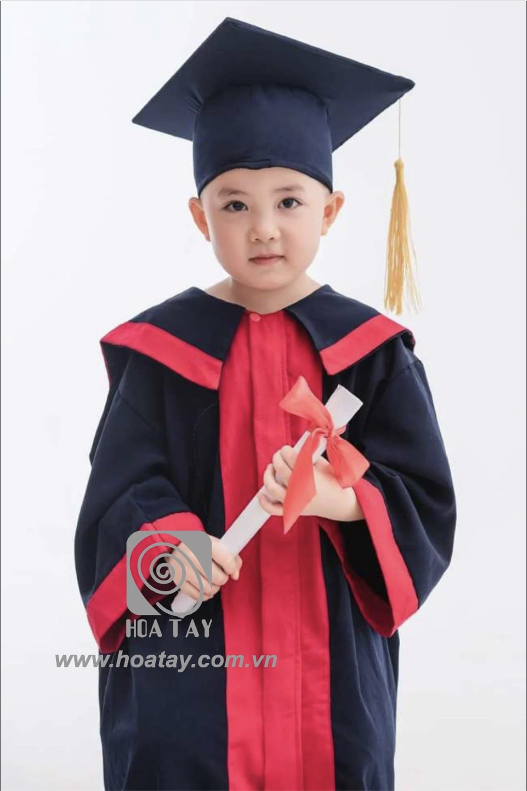 Một bé trai mặc lễ phục tốt nghiệp (áo cử nhân), đội mũ vuông (mũ tốt nghiệp) có tua rua vàng, cầm bằng chứng nhận cuộn tròn buộc nơ đỏ; áo choàng xanh đen phối viền đỏ, chất liệu vải thô, phông nền t