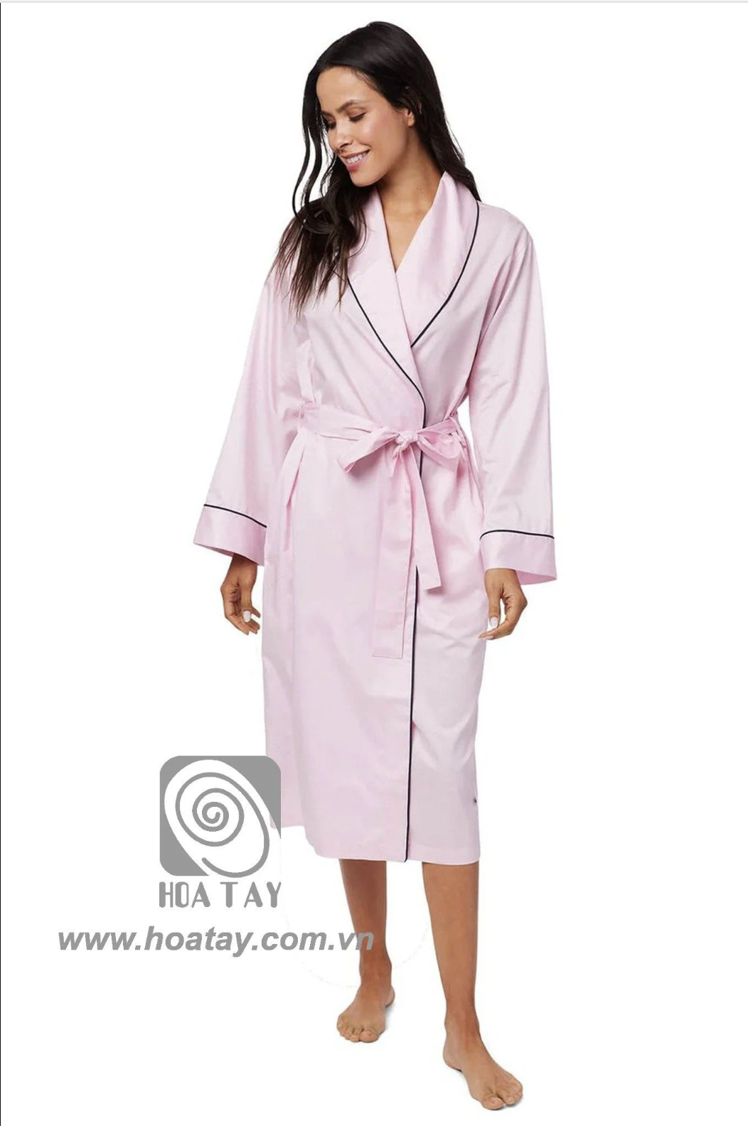 Một phụ nữ đang đứng, mặc áo choàng tắm (bathrobe) màu hồng nhạt, chất liệu cotton, cổ áo kiểu khăn choàng (shawl collar) có viền đen, tay áo rộng, thắt đai eo, nền trắng, ánh sáng studio.