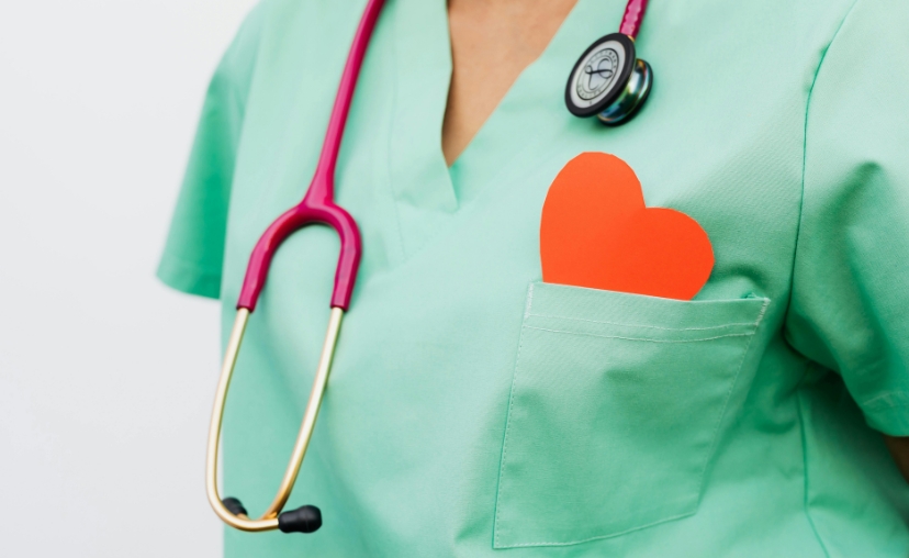 Một thân người y tá -> mặc áo blouse màu xanh lá cây nhạt, cổ V, tay ngắn -> ống nghe màu hồng với đầu kim loại vàng đeo trên cổ -> một hình trái tim màu cam nhô ra từ túi áo ngực -> phông nền trắng s
