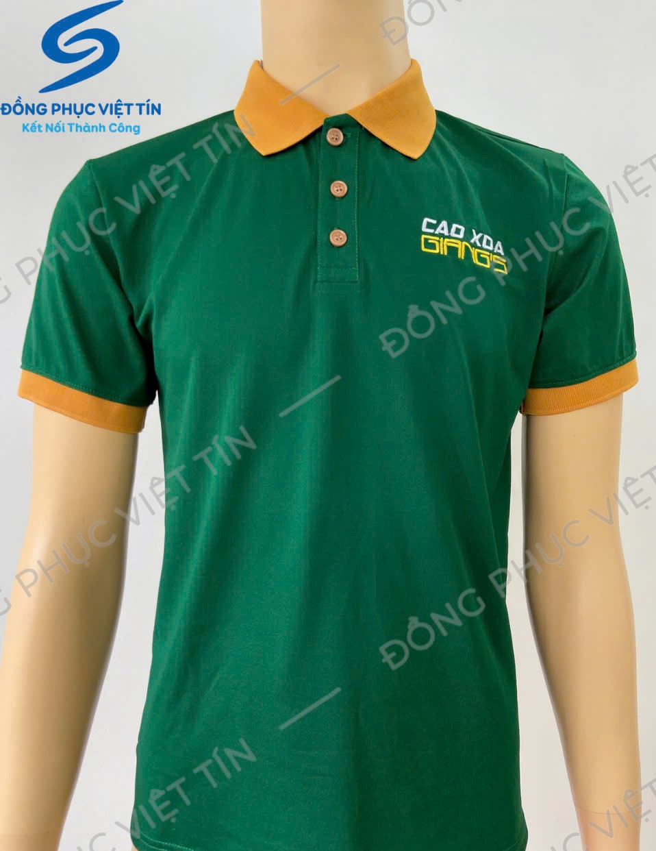 Áo polo màu xanh lá cây với cổ và bo tay màu vàng cam, chất liệu Poly cao cấp, mặc trên ma-nơ-canh. Logo thêu trên ngực trái.
