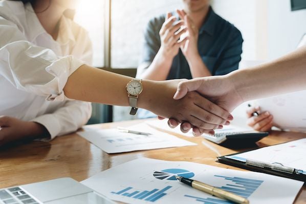 alt: Two hands shaking over a table, symbolizing partnership