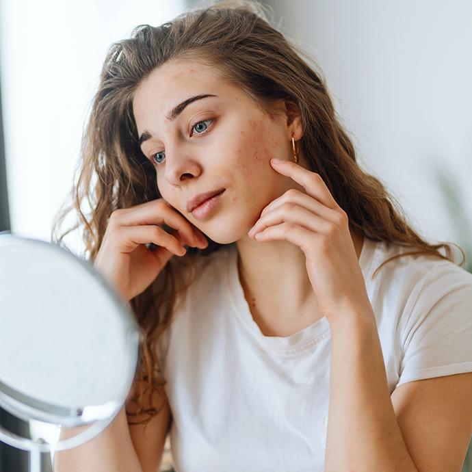 Cô gái trẻ đang nhìn vào gương, thể hiện sự quan tâm đến tình trạng da và routine chăm da đơn giản mà hiệu quả.