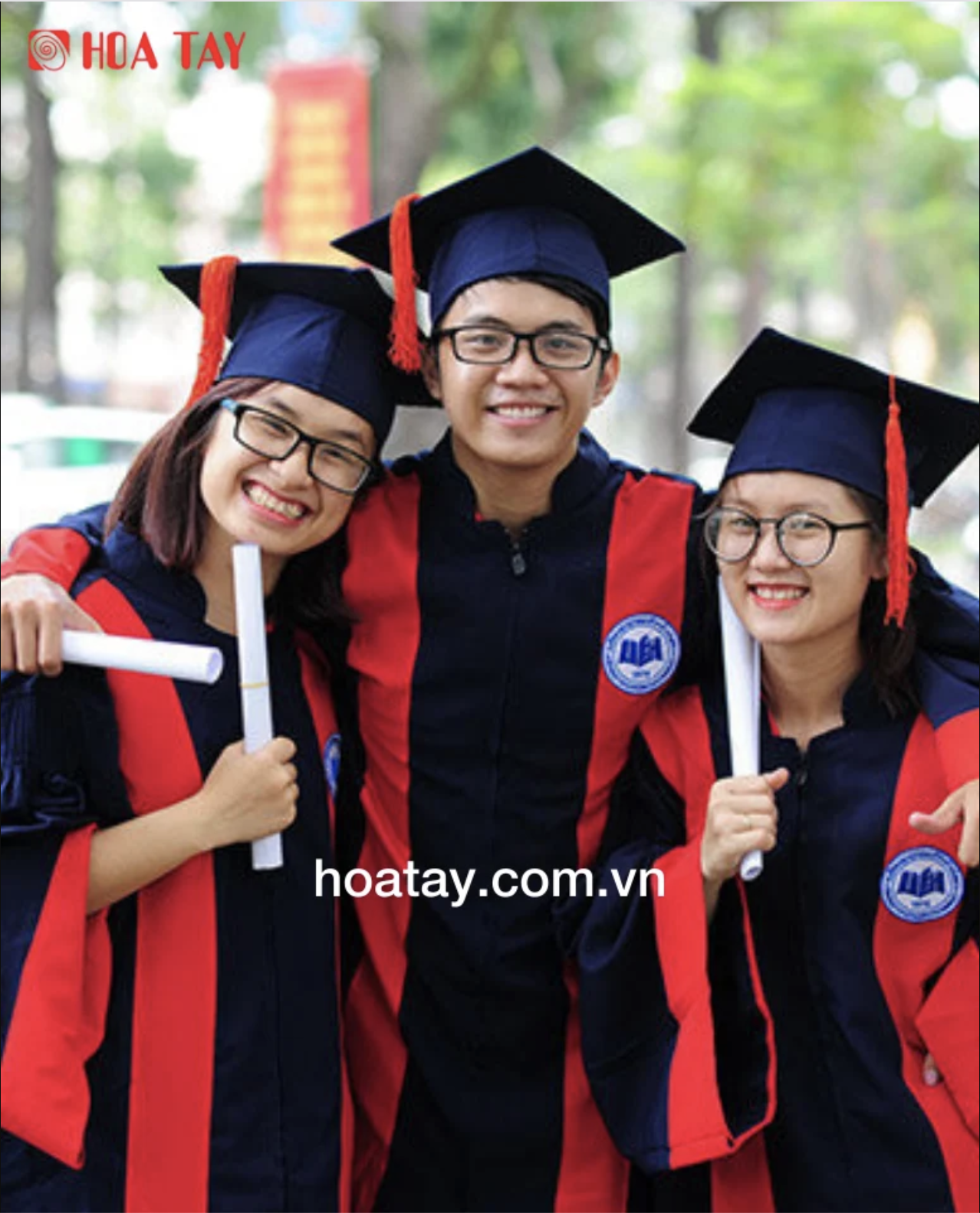 Ba sinh viên (một nam, hai nữ) đang ôm nhau cười tươi; mặc lễ phục tốt nghiệp (áo cử nhân) màu xanh đen phối đỏ, mũ vuông (nón tốt nghiệp) có tua rua, cầm bằng tốt nghiệp cuộn tròn; bối cảnh ngoài trờ