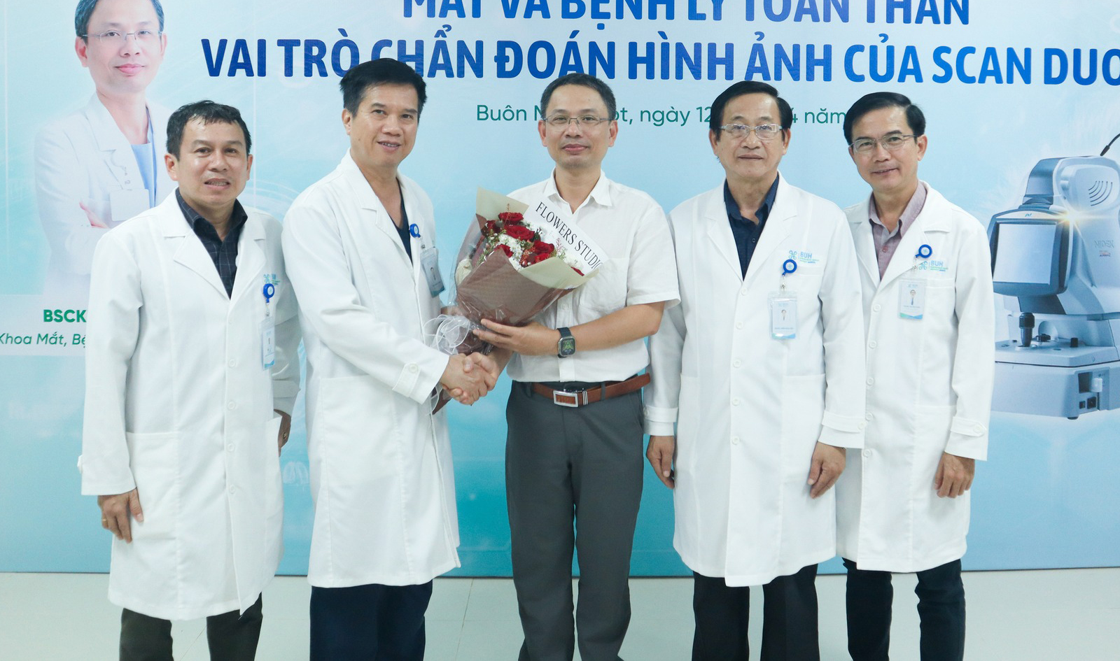 Năm người đàn ông (năm nhân vật) đang bắt tay và trao hoa; mặc áo blouse trắng (áo khoác y tế) dài tay, cổ bẻ, chất liệu vải cotton, có bảng tên và logo gắn ngực; bối cảnh hội thảo y khoa với phông nề