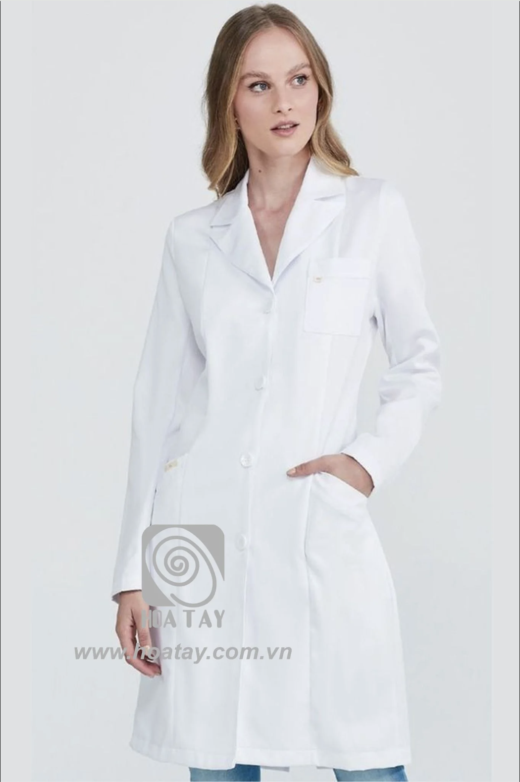 Một nữ bác sĩ mặc áo blouse trắng (áo khoác phòng thí nghiệm) dài tay, cổ bẻ (cổ ve), cài khuy đơn (hàng nút dọc), chất liệu vải cotton dày dặn, có túi ngực và túi hông, phông nền studio sáng.